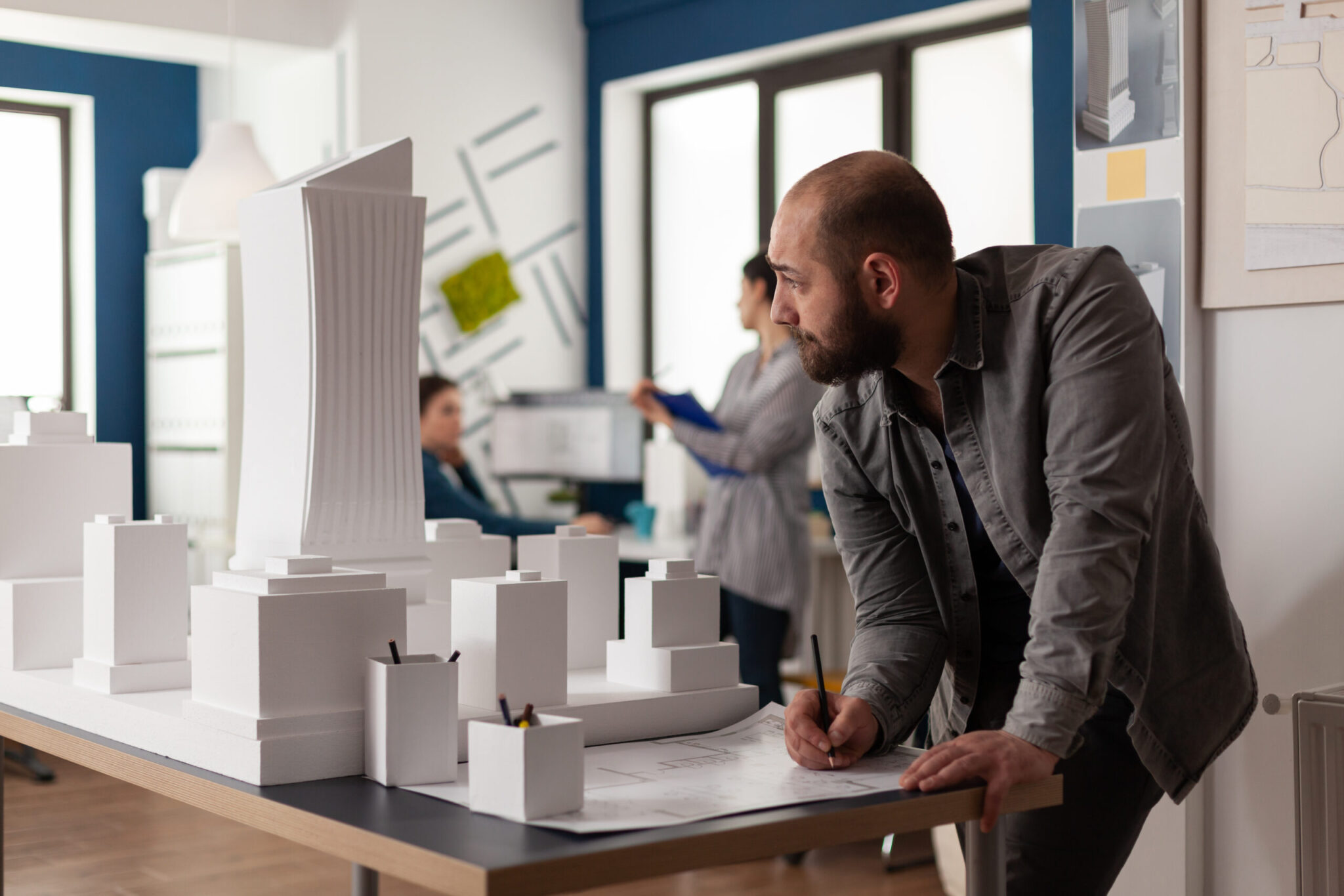 Man working on architectural design at office while looking at laptop computer for industry construction. Project manager inspecting maquette modern design building model